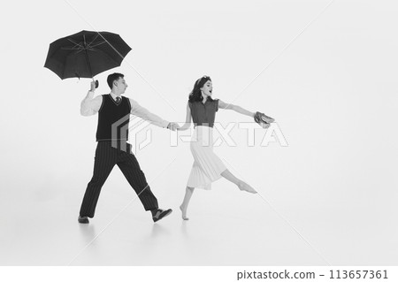 Charming young couple, dressed in vintage attire, holding hands and cheerfully walking under umbrella isolated on white background 113657361