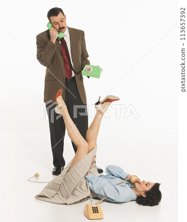 Positive and relaxed young woman lying on floor while man in suit standing and talking on phone. Diversity of emotions. Positive and relaxed young woman lying on floor while man in suit standing and talking on phone. Diversity of emotions. 113657392