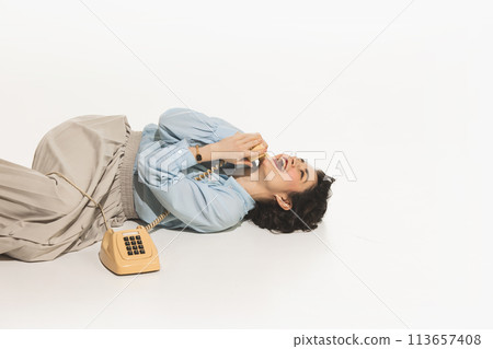 Happy, emotional, young woman lying on floor and talking on retro style phone, having fun on conversation, isolated on white 113657408