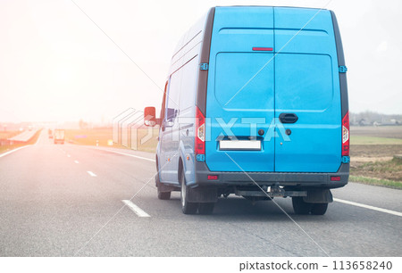 A blue manufactured goods van transports non-food cargo along a highway in the spring against the backdrop of the sun, copy space for text, industry 113658240