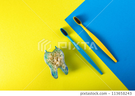 Blue and yellow toothbrush with hard bristles and charcoal coating on a yellow-blue background next to a tooth model. Prevention of caries and cleaning of teeth and oral cavity in dentistry. Fresh 113658243