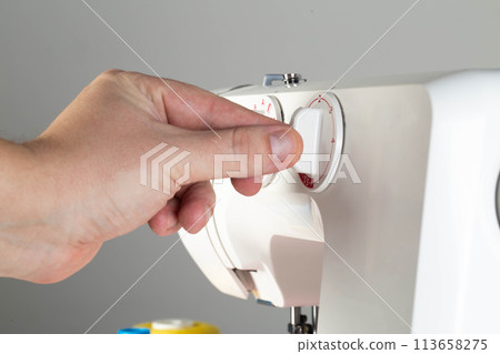 The hand of a seamstress switches the stitch regulator on a sewing machine while sewing. Tailoring services, close-up. Industry The hand of a seamstress switches the stitch regulator on a sewing machine while sewing. Tailoring services, close-up. Industry 113658275