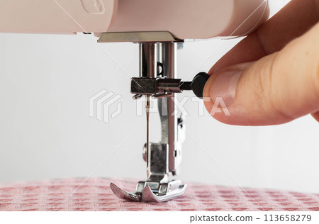The fingers of a seamstress unscrew the needle holder of a sewing machine needle, close-up. Copy space for text, automatical The fingers of a seamstress unscrew the needle holder of a sewing machine needle, close-up. Copy space for text, automatical 113658279