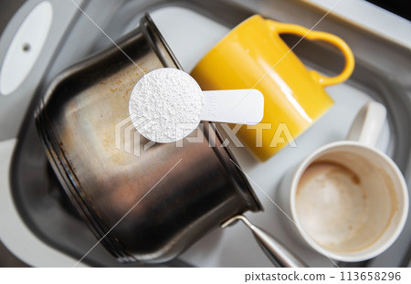 measuring spoon with granules of environmentally friendly oxygen bleach in a basin with dirty dishes. Cleaning grease and dirt from dishes, close-up 113658296