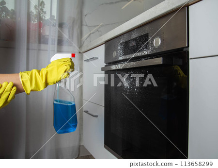 A girl holds a blue spray in her hand against the background of a modern electric oven in the kitchen. Concept for caring and cleaning an electric stove. Care of household appliances, cleaning A girl holds a blue spray in her hand against the background of a modern electric oven in the kitchen. Concept for caring and cleaning an electric stove. Care of household appliances, cleaning 113658299