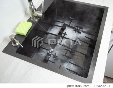 Dirty gas stove grates in the sink with a modern oxygen cleaner for kitchen cleaning. Cleaning the kitchen, removing grease stains, close-up 113658304