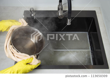 Man's hands in yellow gloves pour pots of hot water into a sink with dirty filters from the hood in the kitchen. Cleaning from dirt and grease with an oxygen cleaner. Copy space for text 113658309