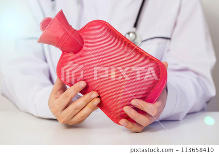 The doctor is holding a red heating pad with hot water in his hands. The concept of heat treatment, muscle relaxation, spasm relief, close-up The doctor is holding a red heating pad with hot water in his hands. The concept of heat treatment, muscle relaxation, spasm relief, close-up 113658410