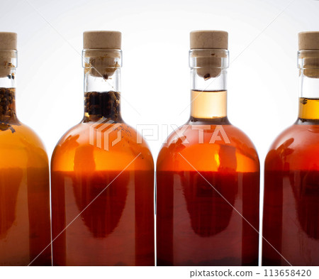 Bottles with transparent brown alcoholic drink on a white background. Homemade herbal tincture of herbal moonshine. Elite alcohol. Bottles with transparent brown alcoholic drink on a white background. Homemade herbal tincture of herbal moonshine. Elite alcohol. 113658420