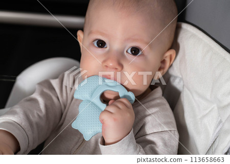 A child aged one year bites a blue medical teether. Concept massager for gums during teething in children. Excessive salivation, close-up 113658663