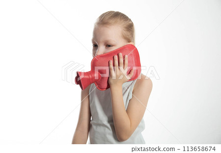 A little girl applies a heating pad with warm water to her neck for neck pain and toothache. Heat treatment 113658674