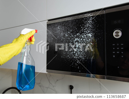 Anti-grease spray in the hand of a girl who is cleaning the kitchen. Cleaning the microwave oven from grease and dirt. Modern antistatic agent. Cleaning company services 113658687