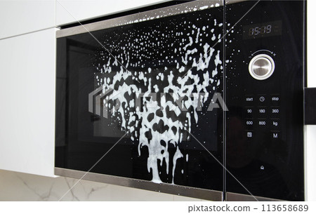 Foam on the microwave screen in the kitchen. The concept of cleaning household kitchen appliances from grease and dirt, close-up 113658689