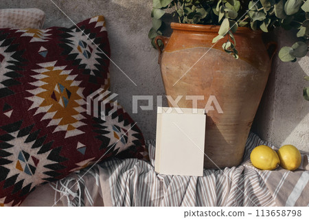 Blank greeting card, invitation mockup, craft envelope. Summer vacation still life, relaxation concept. Cozy bench with Mexican pattern cushions. Vase, eucalyptus branches, fresh lemons. Striped plaid 113658798