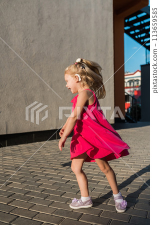Child with hearing problem and cochlear implant dance in street, deaf kid began to hear. Hearing loss in childhood and treatment concept. Copy space and empty place for text. Inclusion 113659585