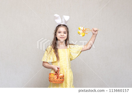 A girl with rabbit ears on her head holds a bouquet of yellow eggs in her hands. Easter for a child. A girl with rabbit ears on her head holds a bouquet of yellow eggs in her hands. Easter for a child. 113660157