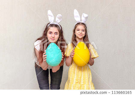 Happy Easter. Two girls wearing Easter bunny ears hold Easter eggs in their hands. Copy space. 113660165
