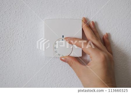 Human hand turns off the heating at home. Central Heating thermostat control dial adjustment 113660325