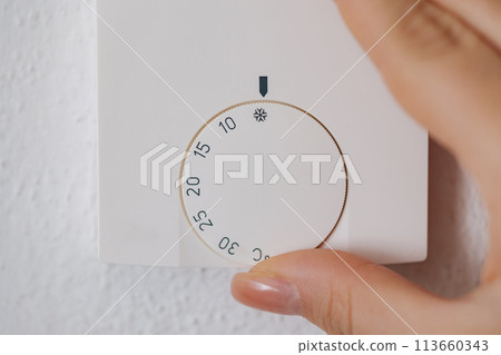 Close-up of human hand turns off the heating at home. Central Heating thermostat control dial adjustment. Woman turning down heating thermostat to save money. 113660343