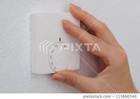 Hand turns down the temperature to 10 degrees Celsius on an electronic thermostat. Symbol for saving energy. An empty house during the holidays 113660348