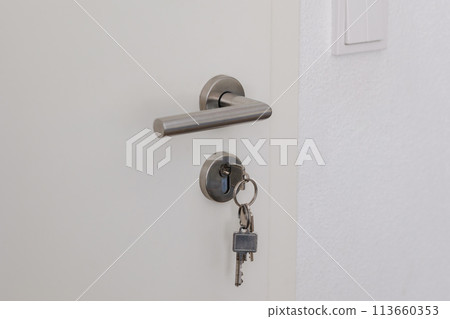 Closed door with keys in the lock. White door and metal handle 113660353
