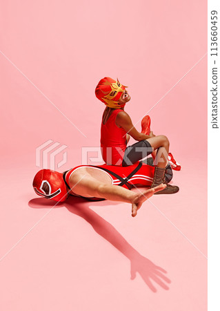Two athletes, man and boy in red outfit with mask playing, fighting against pink studio background. Have fun together Two athletes, man and boy in red outfit with mask playing, fighting against pink studio background. Have fun together 113660459