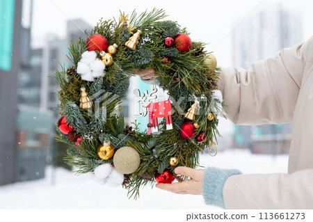 Person Holding Christmas Wreath in Snow 113661273