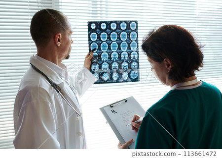 Doctor examining brain computer tomography scan and asking nurse to write out prescription 113661472
