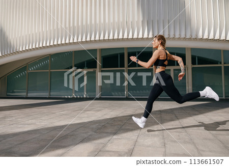 Young woman in sportswear is running on modern buildings background. Active lifestyle concept 113661507