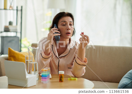 Mature woman in silk pajamas calling doctor before taking any pills Mature woman in silk pajamas calling doctor before taking any pills 113661536