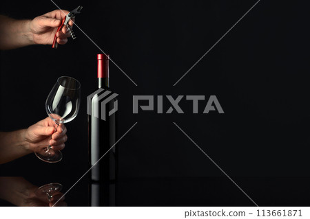 Bottle of red wine and hands with corkscrew and wine glass. 113661871