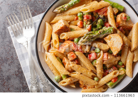 Creamy chipotle chicken penne pasta with asparagus, peppers, green peas, onion and garlic close-up in a bowl. horizontal top view 113661963