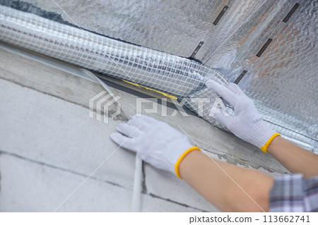 A contractor tapes a vapor barrier between a house and a cold attic. 113662741