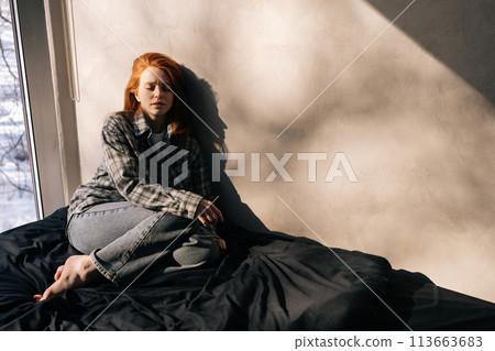 Portrait of depressed young woman sitting on sunny day on floor by window alone, having melancholic mood, troubled with loneliness, upset about solitude mental problem, regret bad mistake concept. Portrait of depressed young woman sitting on sunny day on floor by window alone, having melancholic mood, troubled with loneliness, upset about solitude mental problem, regret bad mistake concept. 113663683