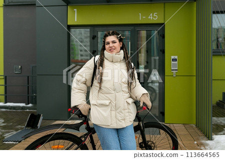 Woman Standing Next to Bike in Front of Building 113664565
