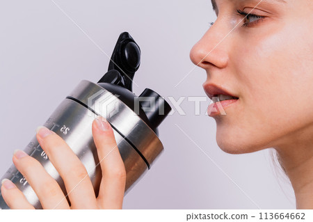 Closeup side view of sportive female after training who drinking fresh water from sport bottle 113664662