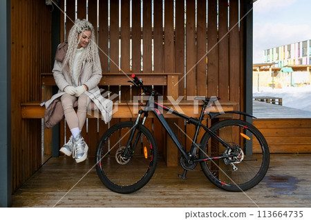 Woman Sitting on Bench Next to Bike 113664735