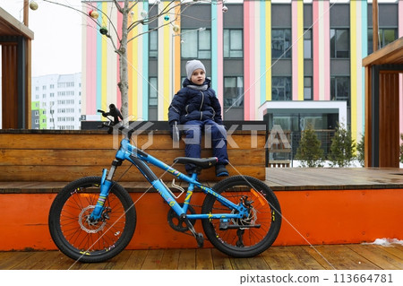 A European boy dressed in a winter jacket gets off his bike 113664781
