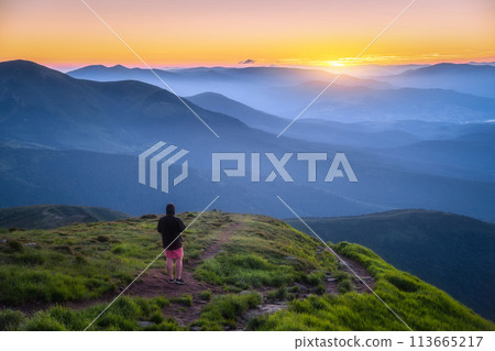 Man on the hill with green grass and mountain valley at sunset 113665217