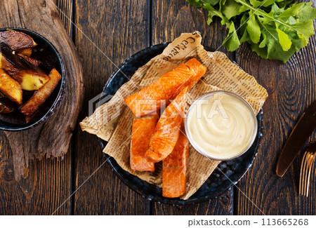 pieces of battered fish on a plate with baked potato on a wooden table with space pieces of battered fish on a plate with baked potato on a wooden table with space 113665268