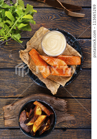 pieces of battered fish on a plate with baked potato on a wooden table with space pieces of battered fish on a plate with baked potato on a wooden table with space 113665269
