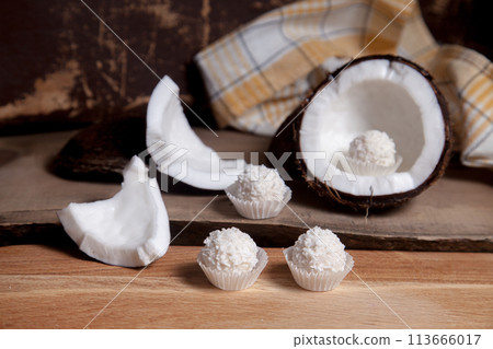 Coconut with white pulp and white candies on wooden background.. Coconut with white pulp and white candies on wooden background.. 113666017