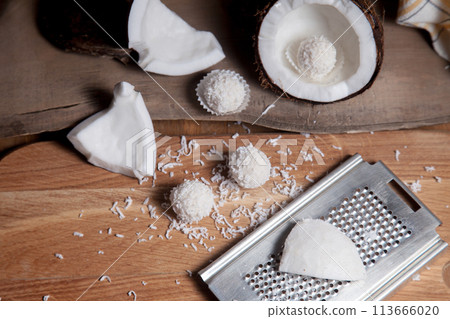 Close up of coconut with white pulp, grater with coconut chip and white candies on wooden background.. 113666020