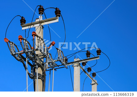 High voltage concrete and steel electrical power post top close up with transformers, ballast, insulators and wires (cables) at pole on a bright blue clear sky background High voltage concrete and steel electrical power post top close up with transformers, ballast, insulators and wires (cables) at pole on a bright blue clear sky background 113666319