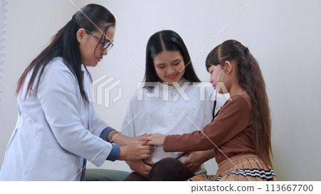 Asian daughter using stethoscope listening baby heartbeat with mother while doctor by side. Asian daughter using stethoscope listening baby heartbeat with mother while doctor by side. 113667700