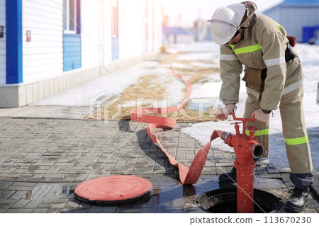 Image of a firefighter connecting a red fire hose to a hydrant for emergency water supply Image of a firefighter connecting a red fire hose to a hydrant for emergency water supply 113670230
