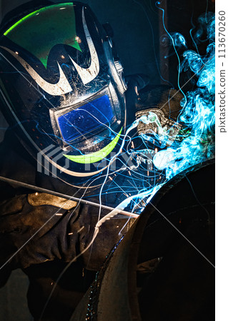 A man wearing a welding helmet is working on a piece of metal. Concept of danger and risk, as the 113670260