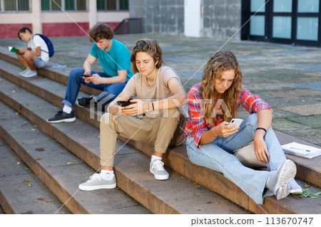 Boy and girl teens sitting on stairs and using smartphones Boy and girl teens sitting on stairs and using smartphones 113670747