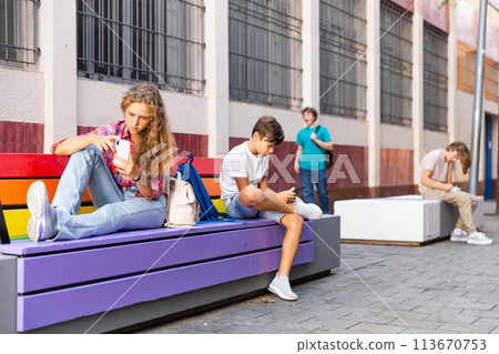 Teenage girl writes message on the smartphone screen while sitting on bench on street 113670753