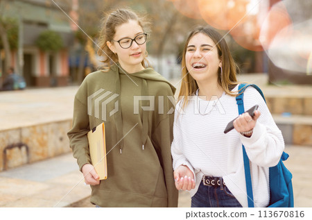 Two cheerful carefree female students walking down street Two cheerful carefree female students walking down street 113670816
